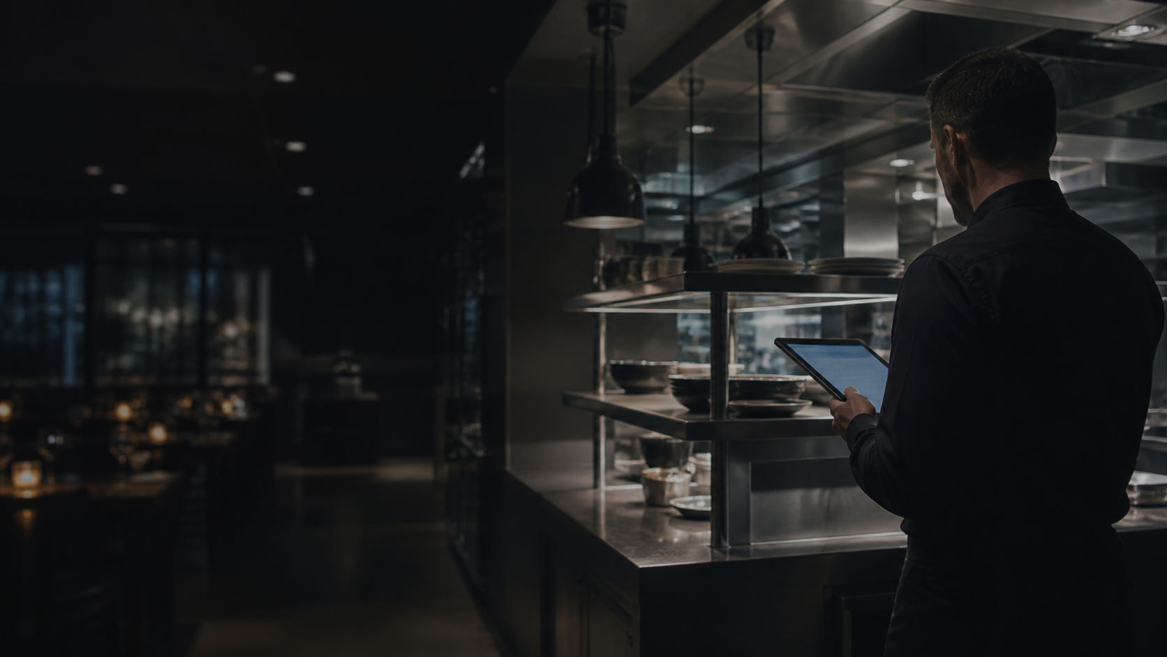 Restaurant operations lead reviewing a tablet beside a busy service pass